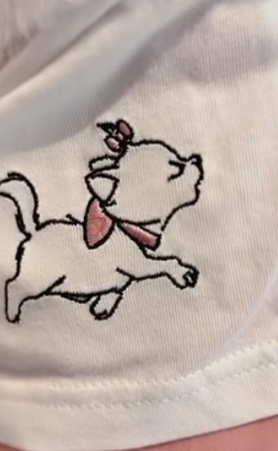 Close-up van Marie (The Aristocats) borduursel met roze strik op witte T-shirtstof – Disney kledingdetail