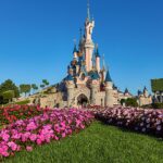 Kasteel van Doornroosje in Disneyland Paris met kleurrijke bloembedden en strakblauwe lucht (zomer 2025)