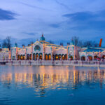 Verlicht historisch gebouw met turquoise koepels weerspiegeld in het water bij schemering in Disney Adventure World Disneyland Paris