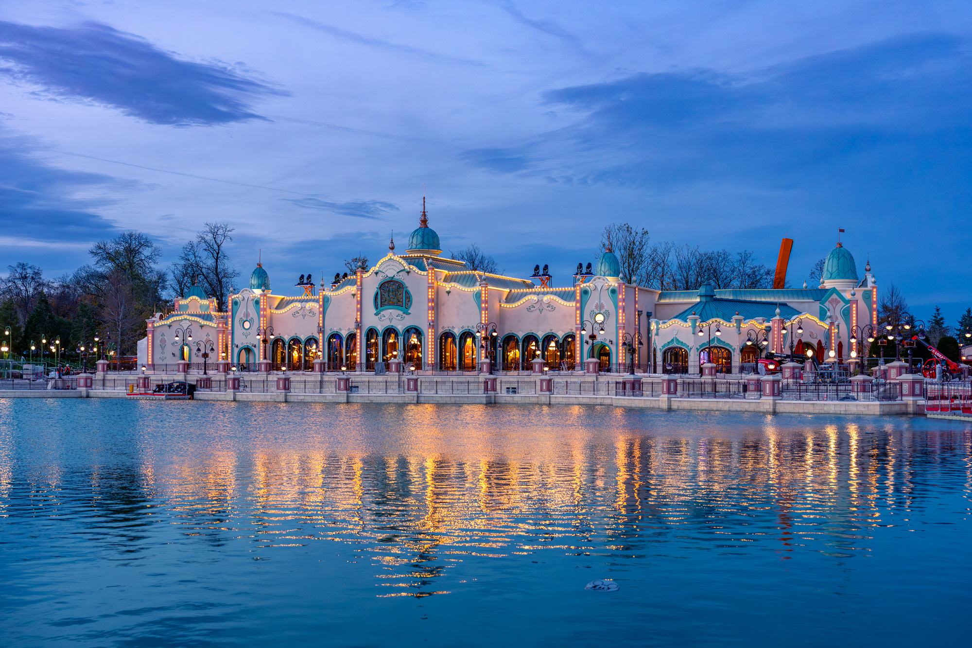 Verlicht historisch gebouw met turquoise koepels weerspiegeld in het water bij schemering in Disney Adventure World Disneyland Paris