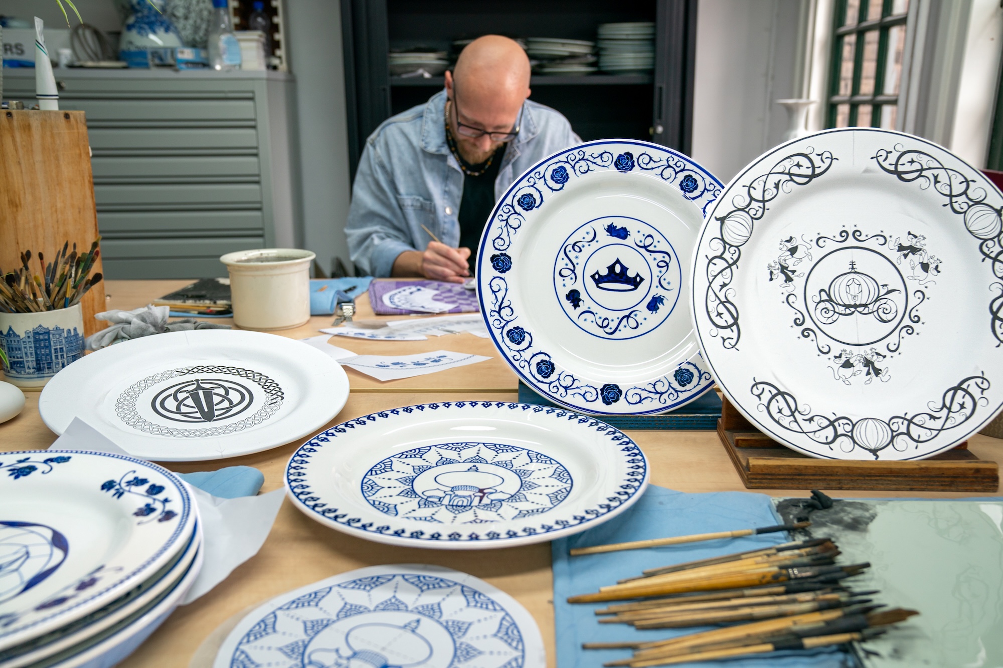 Porseleinschilder bij Royal Delft beschildert borden met Delfts blauwe Disney-patronen in het atelier