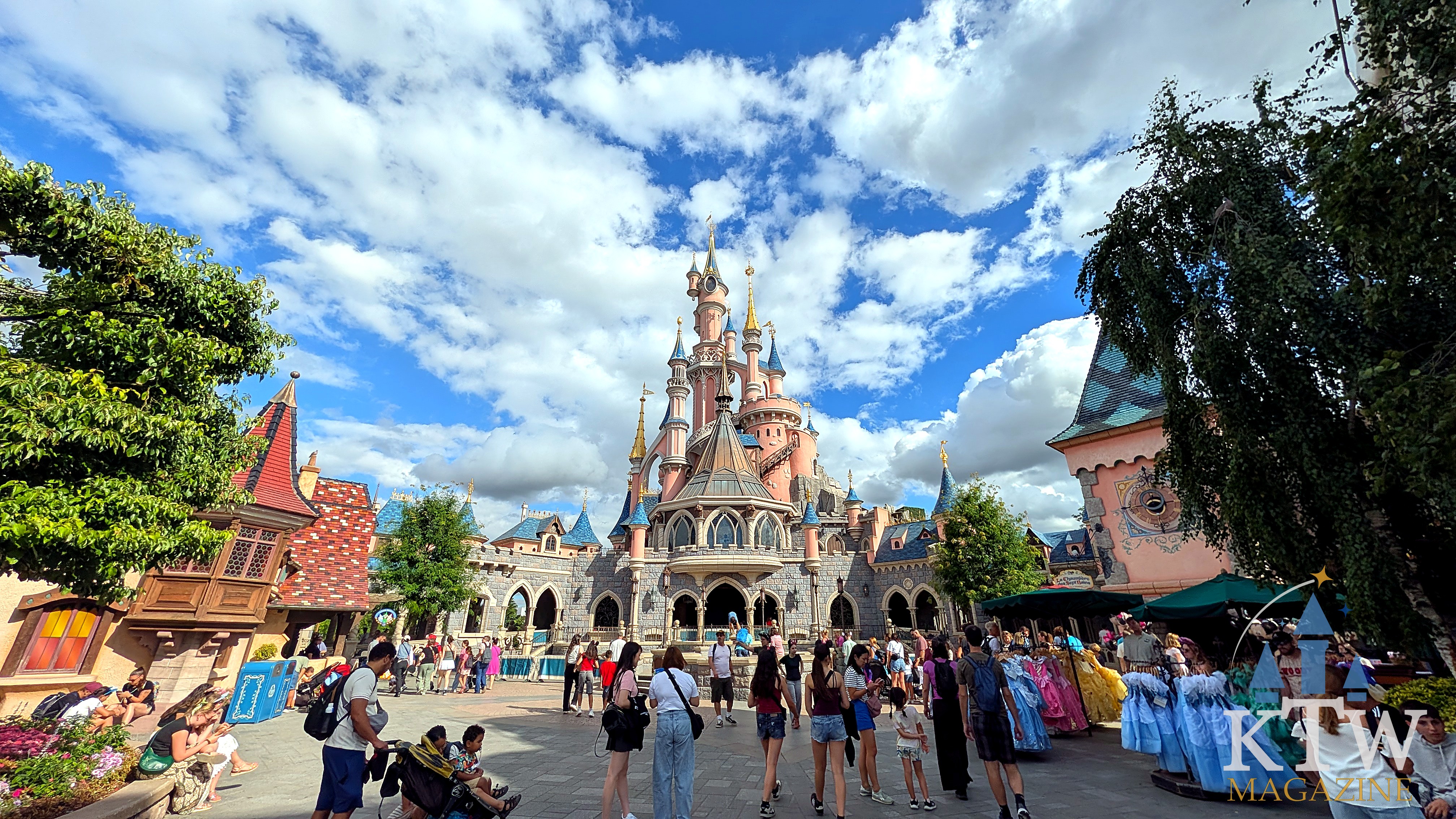 Het roze Kasteel van Doornroosje in Fantasyland, Disneyland Parijs, onder een blauwe lucht met wolken en bezoekers op het plein ervoor